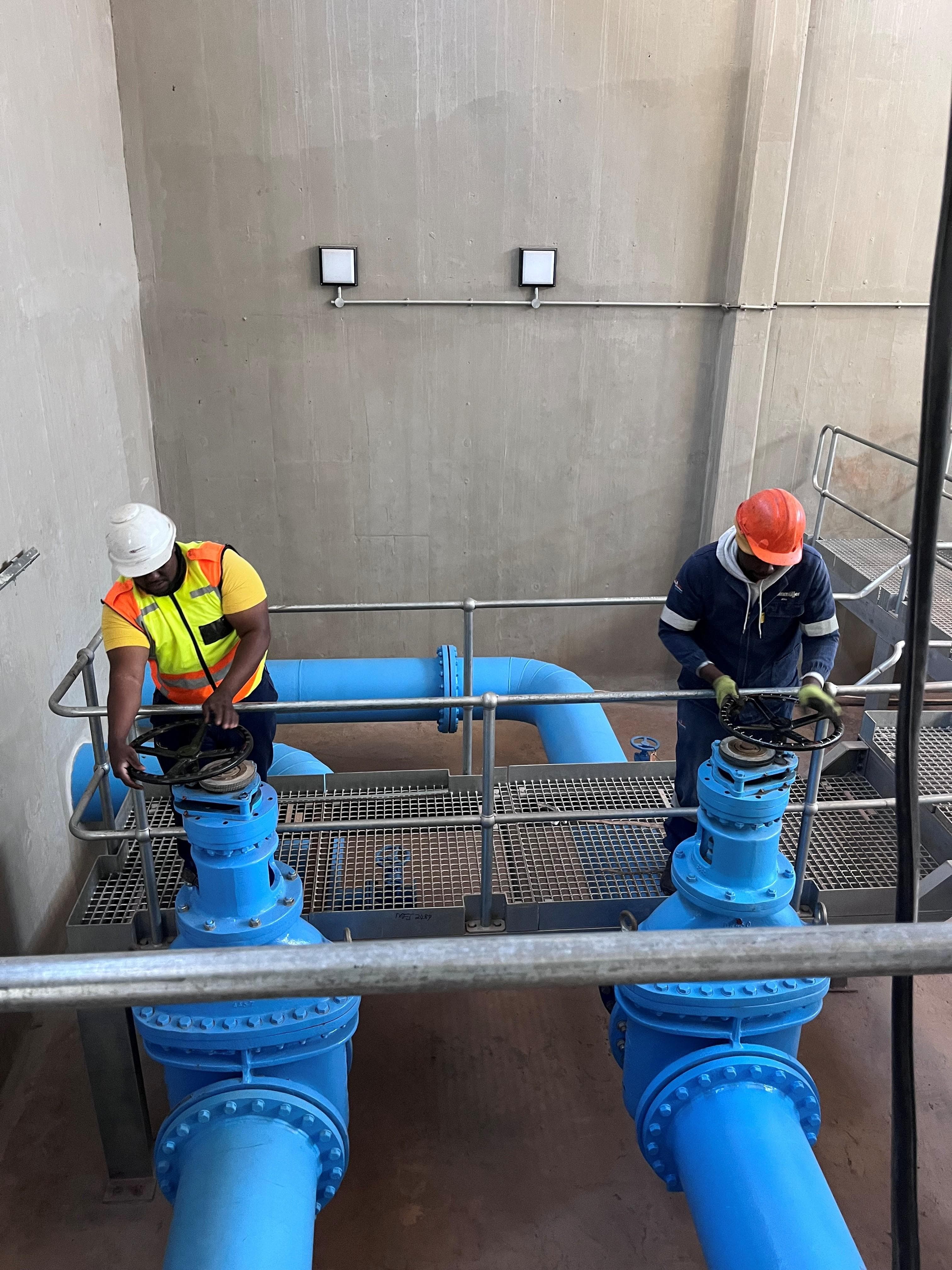 Technicians operating large blue isolation valves on Crosby pump-station pipework
